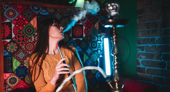 Person exhaling, with hookah wand in hand, in hookah den