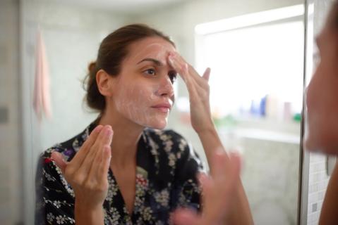 Person in bathroom looking in mirror washing face with fingers