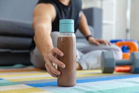 Person reaching for bottle of chocolate milk, dumbbells nearby