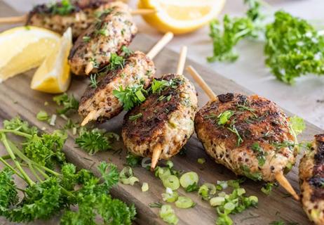 Spiced chicken skewers displayed on a cutting board with green onions and parsley.