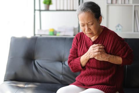 Person seated on sofa, holding chest in pain