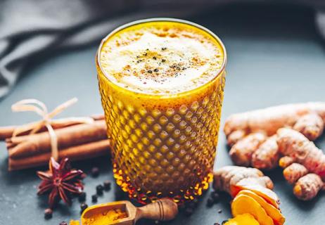 Almond Golden Milk with apricots and cinnamon surrounded by spice ingredients on a dark background.