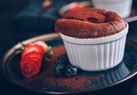 Closeup of a chocolate souffle with strawberry garnish on dark plate.