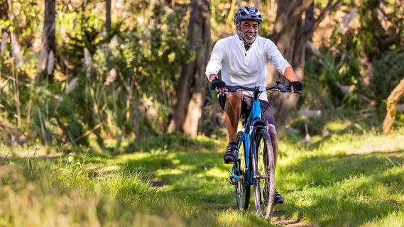 Older male in helmet biking on forest trails