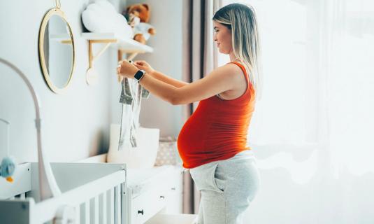 Pregnant person happily folding baby clothes in the nursery