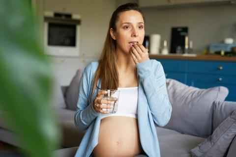Pregnant woman taking allergy pill, with glass of water