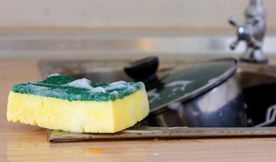 Kitchen sponge sitting on edge of dirty sink filled with dirty pans
