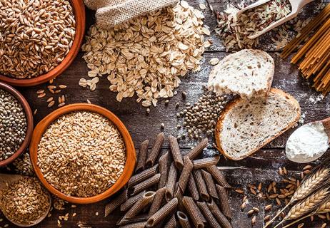 An assortment of dried pasta, wheat, barley, oats, seeds and nuts on a wooden table.