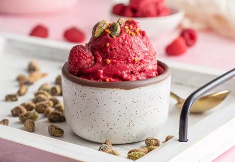 Bowl of dairy-free raspberry coconut ice cream topped with and surrounded by candied pistachios