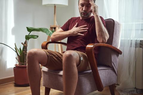 Man sitting in chair, holding hand to chest, trying to relax and breath