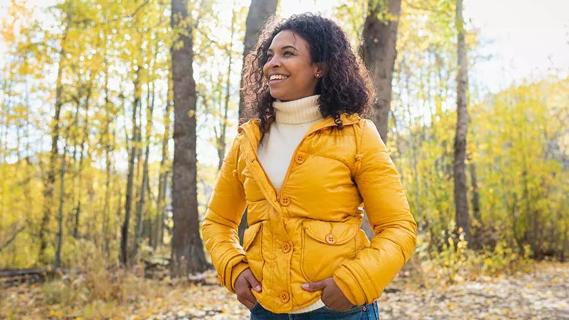 happy female in yellow coat walking in woods