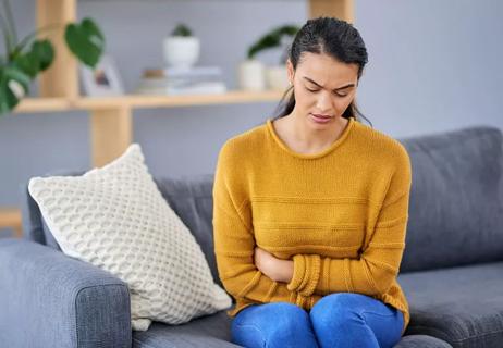 Woman sitting on couch with stomach pain