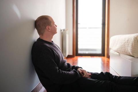 Person sitting on floor, leaning against the wall, looking out the window