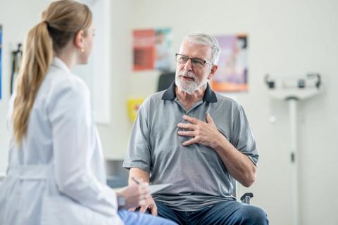 Older man with hand on chest while talking with healthcare provider in exam room