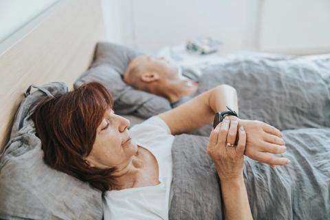 Person waking in bed checking their smartwatch sleep stats, with partner still sleeping