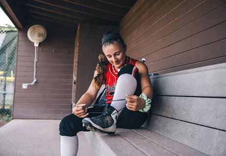 Adolescent female ties cleats before heading to softball