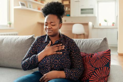 Person sitting on couch wincing, with hand on upper chest