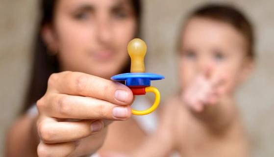Caregiver holding up pacifier and holding baby, who is reaching for the pacifier