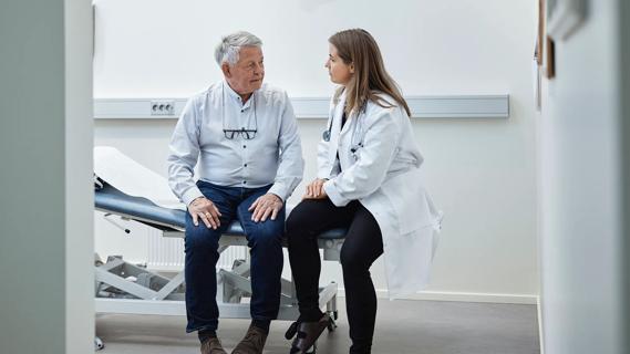 Older man sitting on exam table, talking with healthcare provider