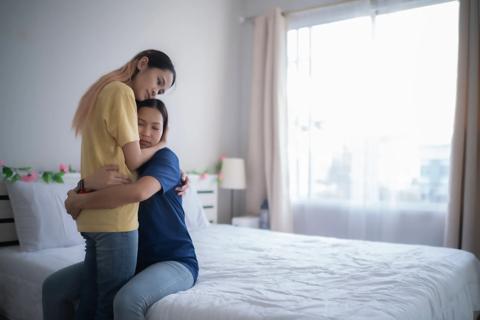 Person sitting on bed hugging person standing