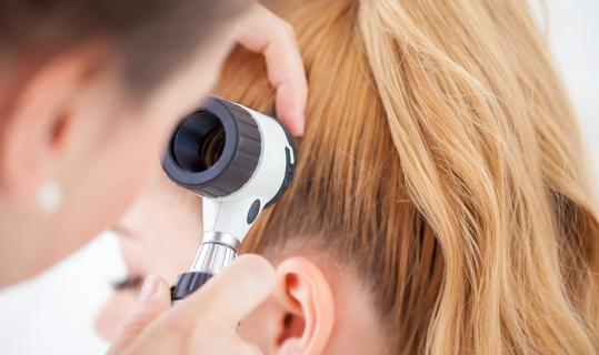 Healthcare provider checking patient's scalp with a trichoscope