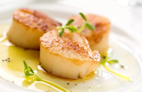 Three large, buttery seared scallops atop olive oil and greens on a white plate