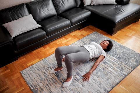 Person doing yoga bridge pose in living room by sofa