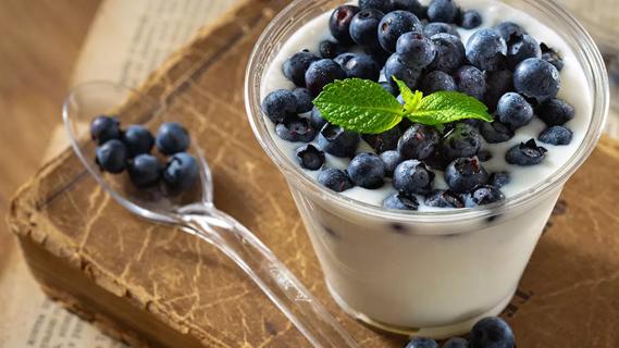 Small cup of yogurt with fresh blueberries on top, with mint sprig