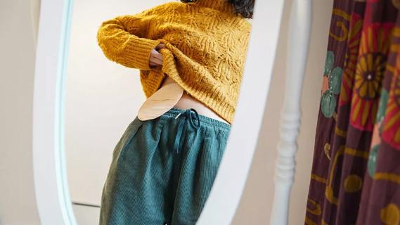 Person lifting up their sweater, showing ostomy bag in mirror's reflection