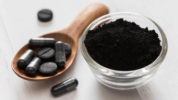 Wooden spoonful of activated charcoal tablets and capsules, and small dish of loose activated charcoal