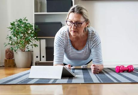 Someone exercising by leaning on their elbows on a striped mat in front of a computer tablet