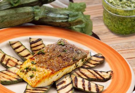 Halibut on slices of grilled zucchini with pesto in background