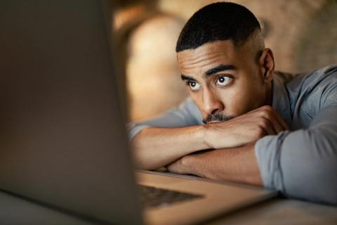 Person with head down on folded arms, staring worriedly into their computer screen