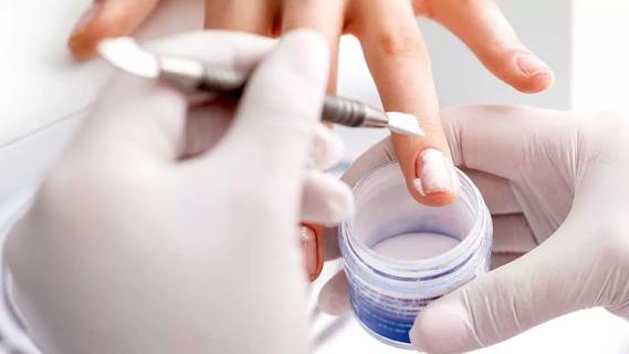 Close up of a woman's hands receiving acrylic powder to nails during manicure