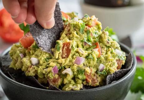 Close-up of a hand dipping a blue-corn tortilla chip into a bowl of guacamole