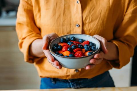 Up close of person's hands holding bowl of strawberries and blueberries over oatmeal