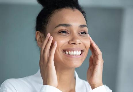 A woman with glowing skin touching her cheeks and smiling