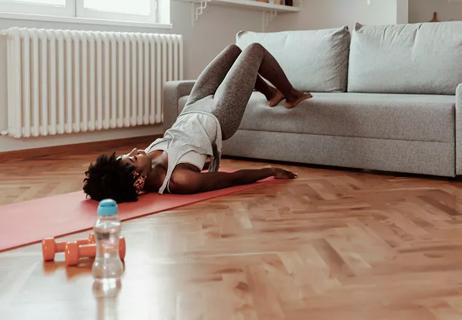 person lying on a yoga mat on the floor doing bridge exercise with their feet on a couch