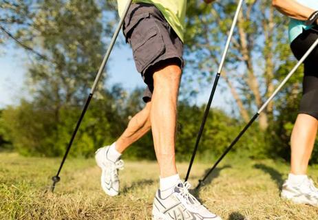 A couple of older adults nordic walking on a grassy trail.