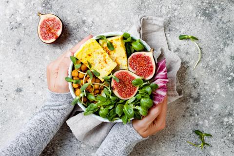 Hands cupping bowl of greens, chickpeas, whole figs, halved and tofu