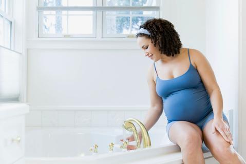 Pregnant woman drawing a bath and testing the temperature with her hand