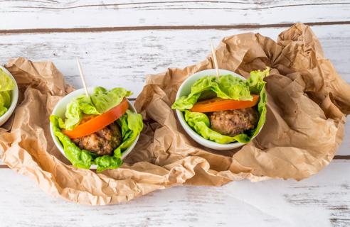 Lettuce-wrapped burgers with tomato, in white bowls atop crumpled brown bag