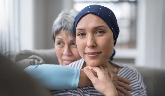 Smiling woman wearing cancer head scarf, with parent hugging her