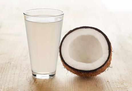 Glass of milky coconut water next to half of an open coconut
