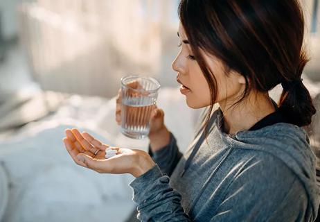 Person holding pills in one hand and a glass of water in the other