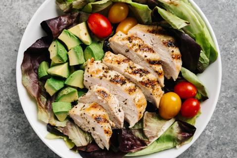 Sliced grilled chicken on greens, with avocado and tomatoes