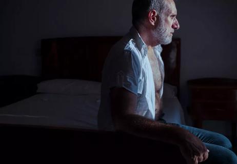 Elder person awake at night sitting on bed in the darkness.