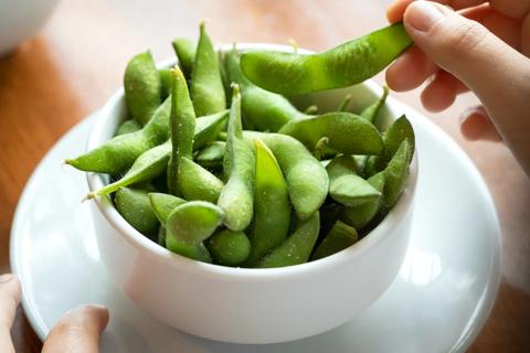 Hand picking up a steamed and lightly salted edamame pod from bowl
