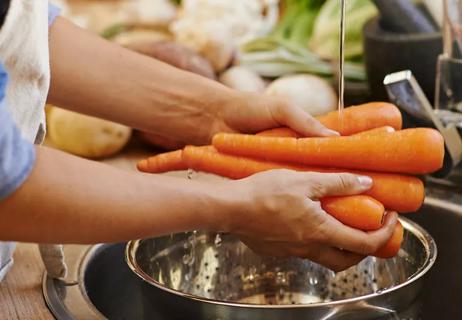 Chef washing carrots under water for food prep