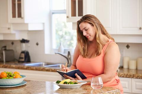 Person sitting at kitchen island with plate of food writing in journal